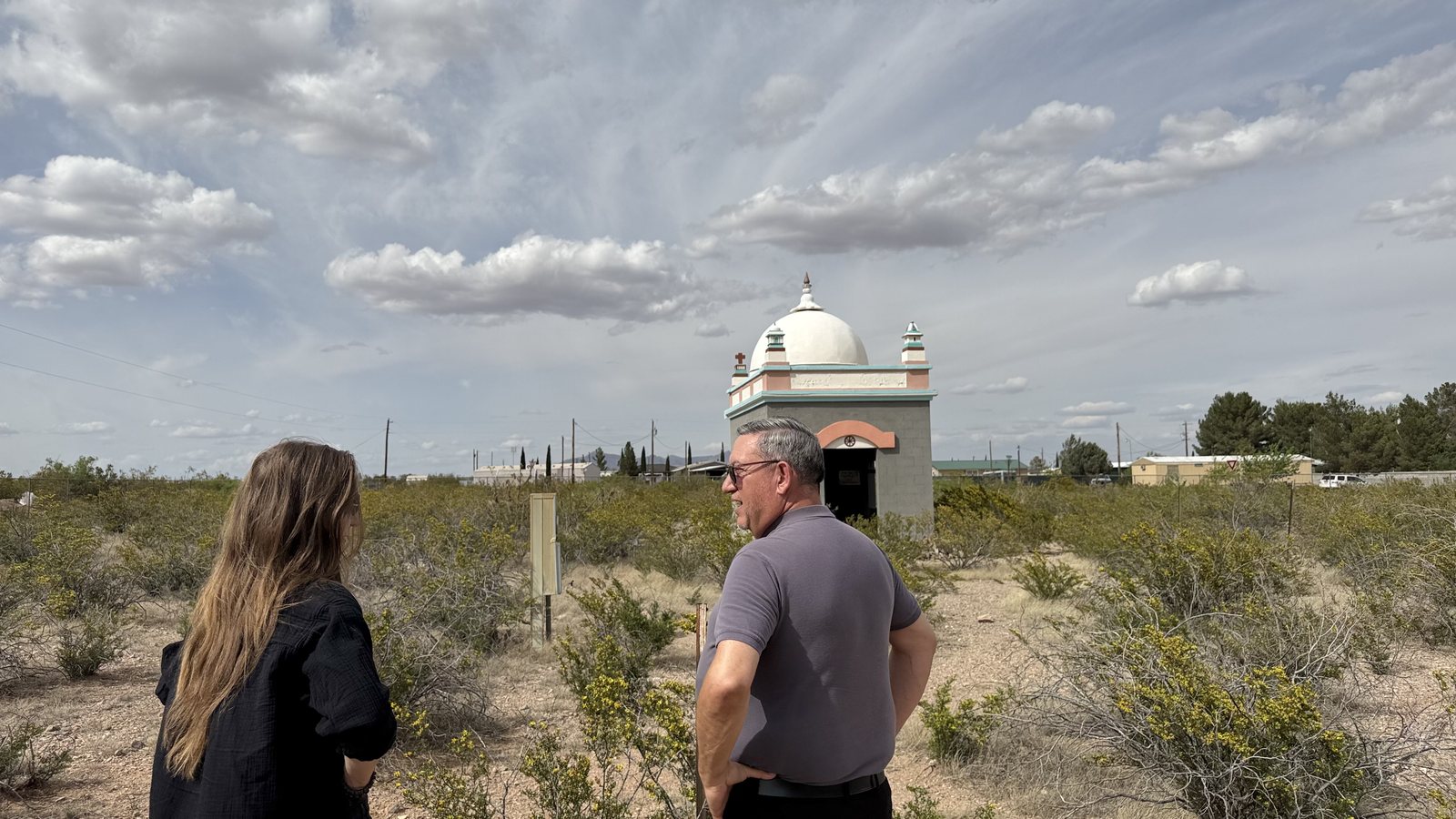 Two people walking a desert path toward the domed shrine